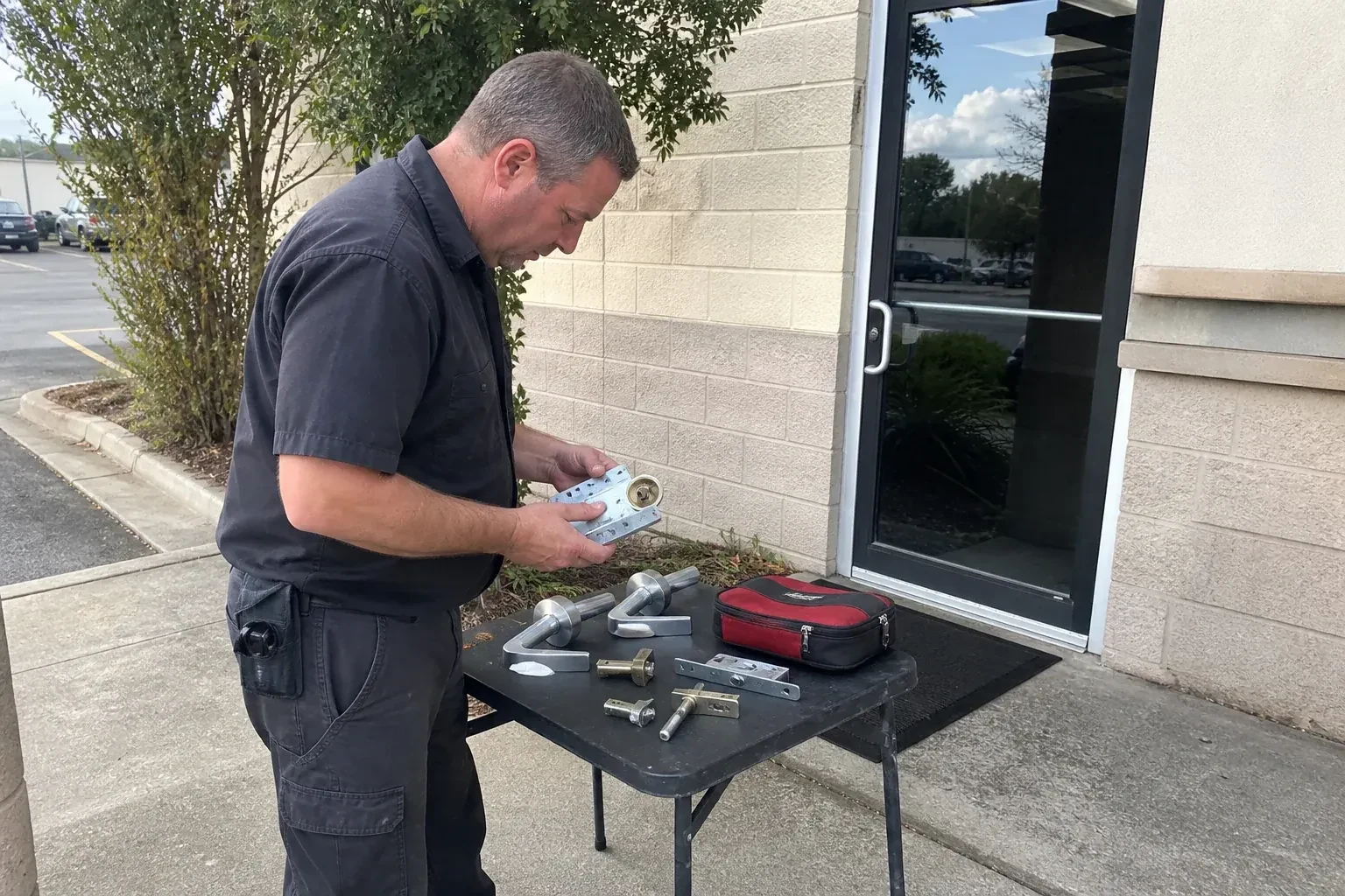 Technician examining detached commercial lock hardware on a table outside a shop entrance. — Business Lockout Service, Kawartha Lakes