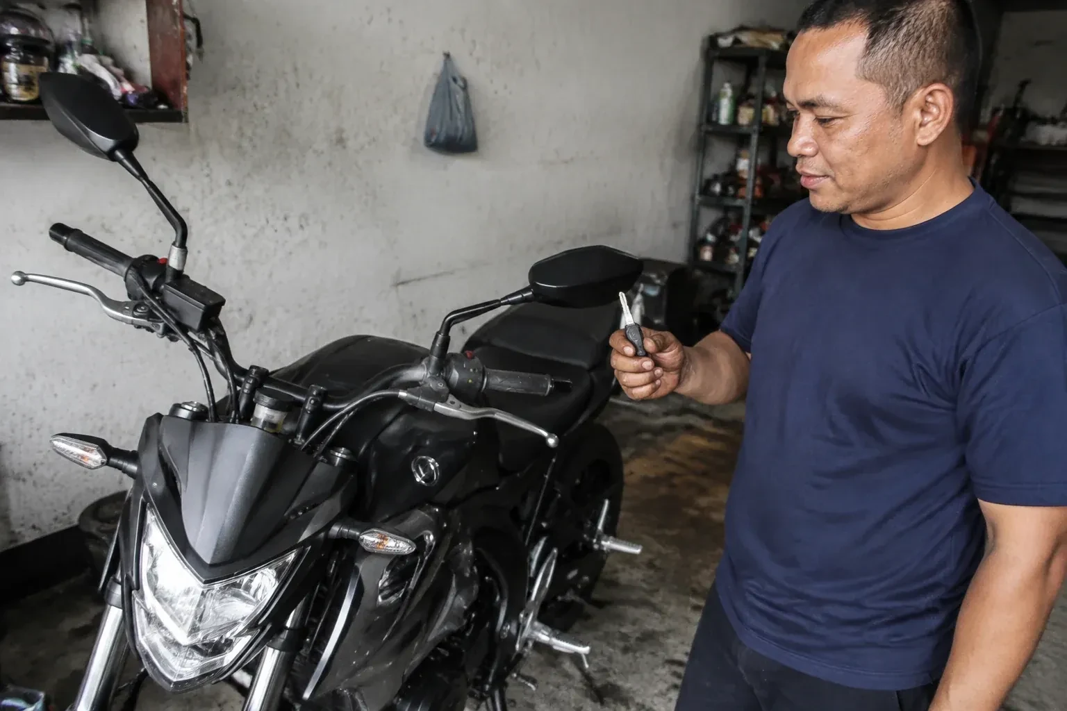Person holding a key beside a black motorcycle in a garage. — Motorcycle & Scooter Keys, Kawartha Lakes
